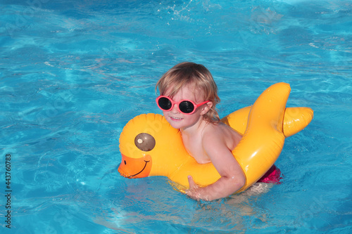 a beautiful cute blond boy in orange glasses is swimming in the pool the sea on a yellow duck lifebuoy is happy and smiling