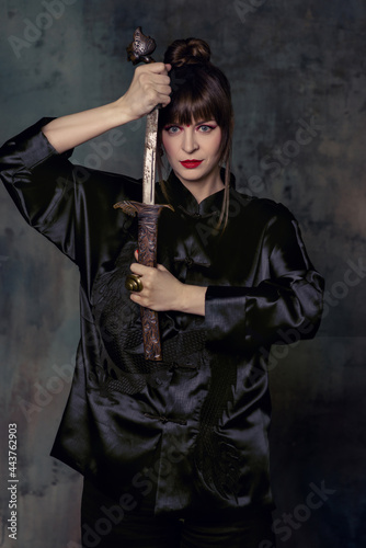 Beautiful woman with bright make up posing in Chinese costume in minimalistic interior with fan and dagger