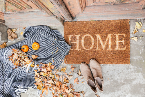 Foto Doormat with plaid, shoes and leaves near entrance of house on autumn day