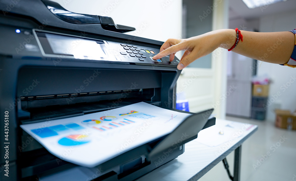 Office worker prints paper on multifunction laser printer. Copy, print, scan,  and fax machine in office. Document and paper work. Print technology. Hand  press on photocopy machine. Scanner equipment. foto de Stock