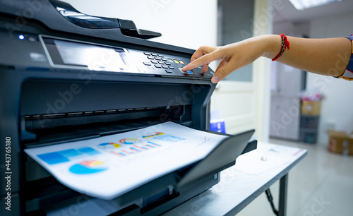 Office worker prints paper on multifunction laser printer. Copy, print, scan, and fax machine in office. Document and paper work. Print technology. Hand press on photocopy machine. Scanner equipment. photo