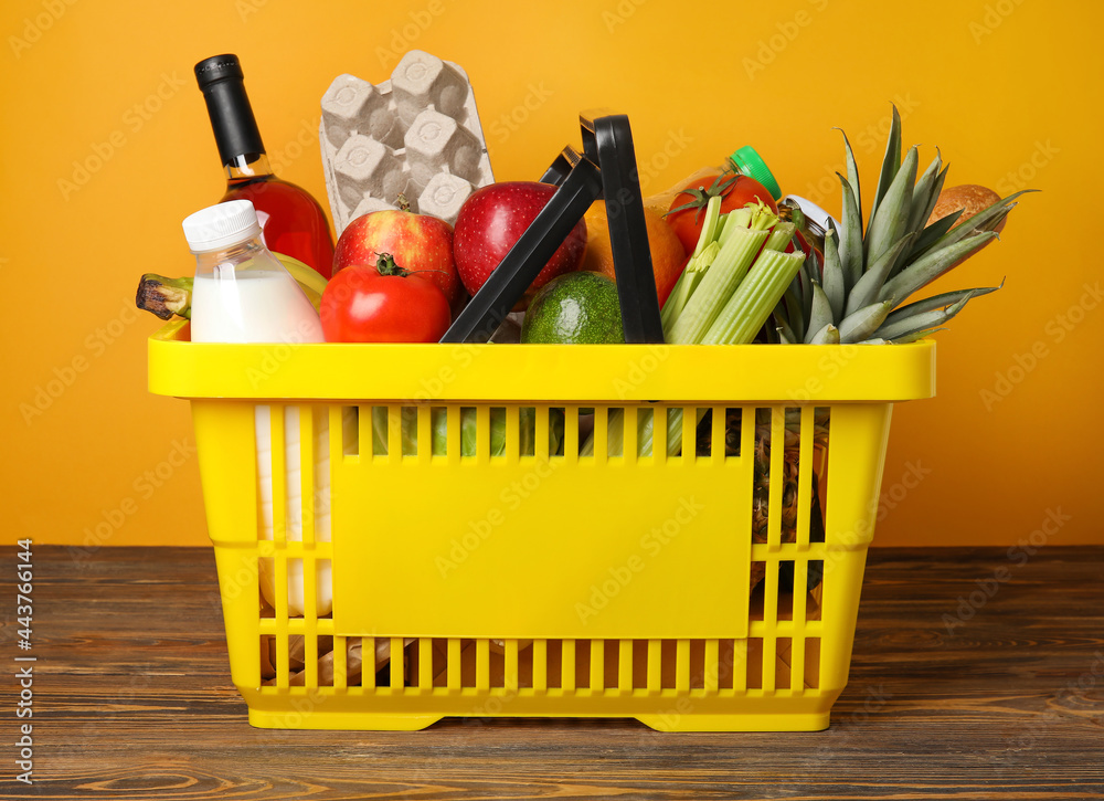 Shopping basket with food on table near color wall