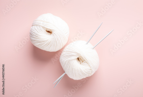 White knitting wool and knitting needles on pastel pink background. Hobby knitting. Top view
