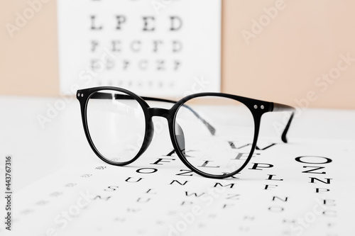 Stylish eyeglasses with eye test chart on table, closeup