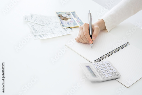 電卓,小銭,レシートを横に置きペンでノートに記入する女性の手のクローズアップ 
