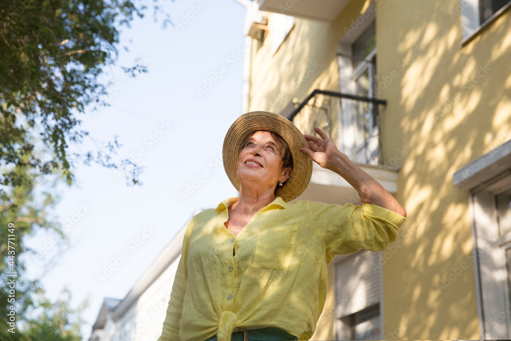 happy senior woman in sun hat walks  on summer city