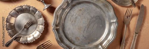 Vintage silver tableware panorama, overhead flat lay shot. Various plates and cutlery on a brown background