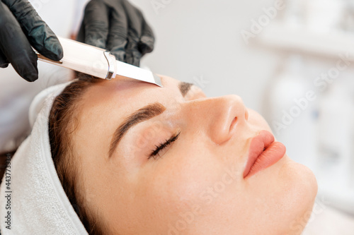 Procedure at the beauty salon. Cosmetologist cleans the client's forehead using a ultrasonic device. Close up. Concept of professional cosmetology