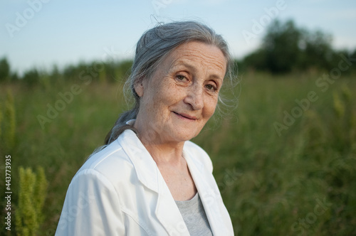 Portrait of senior woman with grey hair and face with wrinkles wearing white jacket and relaxing at park during sunny weather, mothers day