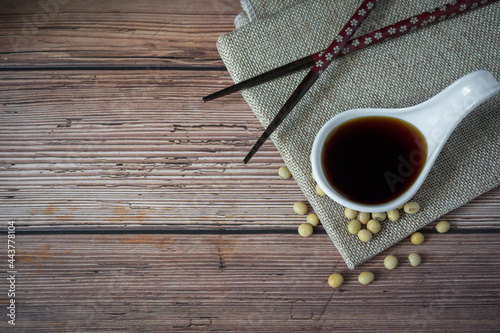 Tasty soy sauce in white ceramic bowl scoop and organic soybean with chopsticks and apron on wood table background.Traditional fermented condiment used in Asia.