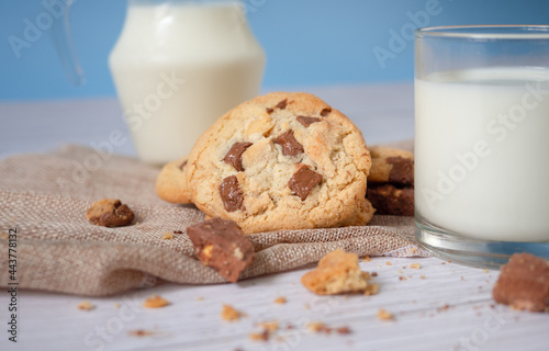 Delicious homemade chocolate chip cookies, paired with fresh milk in a glass and pitcher, placed on a white wooden floor and a blue background cloth. Drink in the morning for health and strong bones.