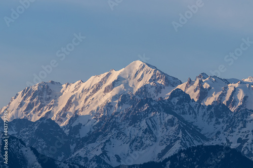 A mountain peak with avalanches and sharp rocks on the ridges, which are illuminated by the sun