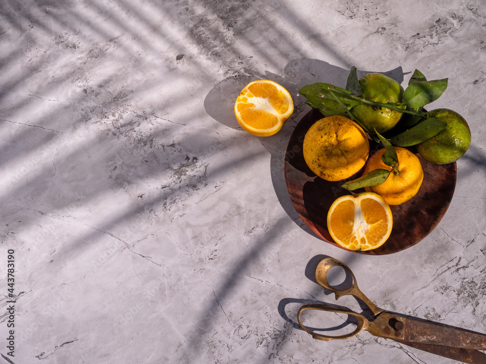 Summer sunny still life. Orange with green foliage on a Plate and white stone background, vintage scissors. Long shadows from a palm branch, neutral color palette. Copy space