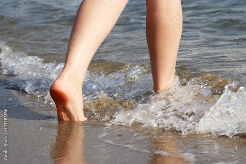 Barefoot woman running by the sand in the sea waves. Naked female legs in water, beach vacation