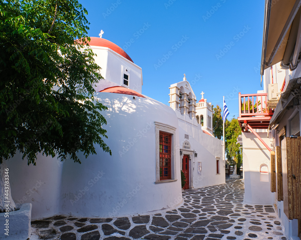 Traditional Greek Orthodox church in Greek island town. Red dome, whitewashed walls, Greek flag and bell tower. Mykonos, Cyclades, Greece. Traditional Greek Orthodox church in Greek island town. Red dome, whitewashed walls, Greek flag and bell tower. Mykonos, Cyclades, Greece.
