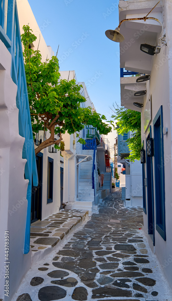 Beautiful traditional alleyways of Greek island towns. White walls, blue balconies and doors, cobblestone street, morning sun. Mykonos, Greece