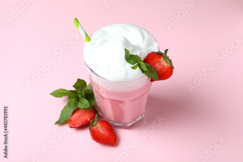 Glass of strawberry milkshake and ingredients on pink background