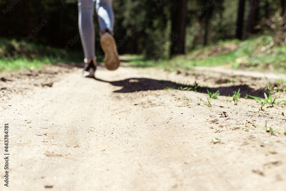 Rear view photo of female tourist legs walking in a forest road.Summer day.Selective focus. Rear view photo of female tourist legs walking in a forest road.Summer day.Selective focus.