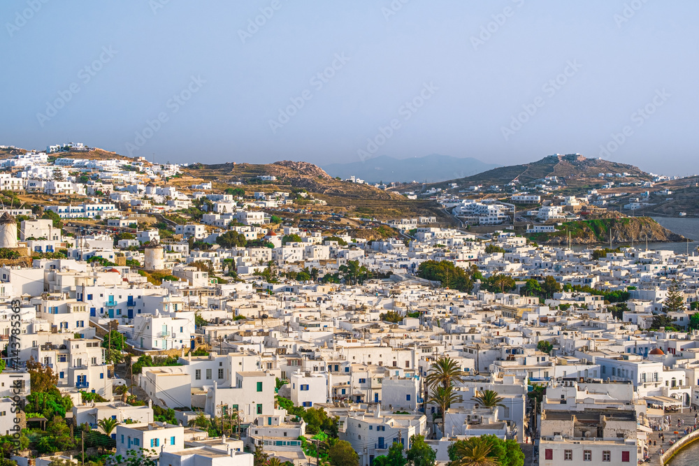Beautiful view of Chora town of Mykonos at sunset, Greece. Whitewashed houses, hills, greenery, seafront, famous windmills. 