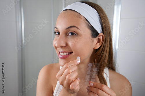 Beautiful smiling girl applying acne treatment patch on a pimple in bathroom