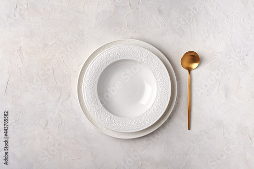 Empty white plate and golden spoon. Kitchen utensils set on light gray table. Top view flat lay with copy space