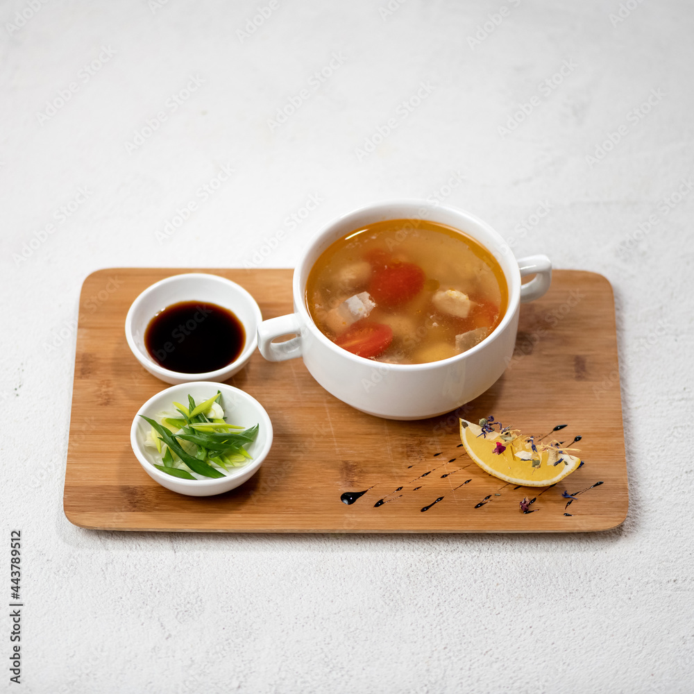Poultry meat soup with tomatoes and lemon, soy sauce and chopped onions on wooden cutting board. Beautiful serving of food. Object isolated on white background. Poultry meat soup with tomatoes and lemon, soy sauce and chopped onions on wooden cutting board. Beautiful serving of food. Object isolated on white background.