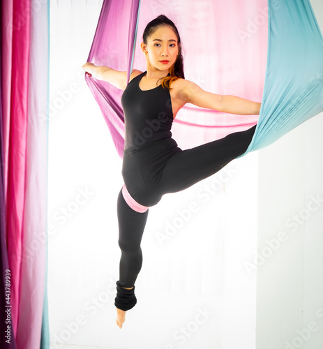 Young beautiful Asian dancer dressed in black color performing aerial dance with multi-color fabrics in the studio..