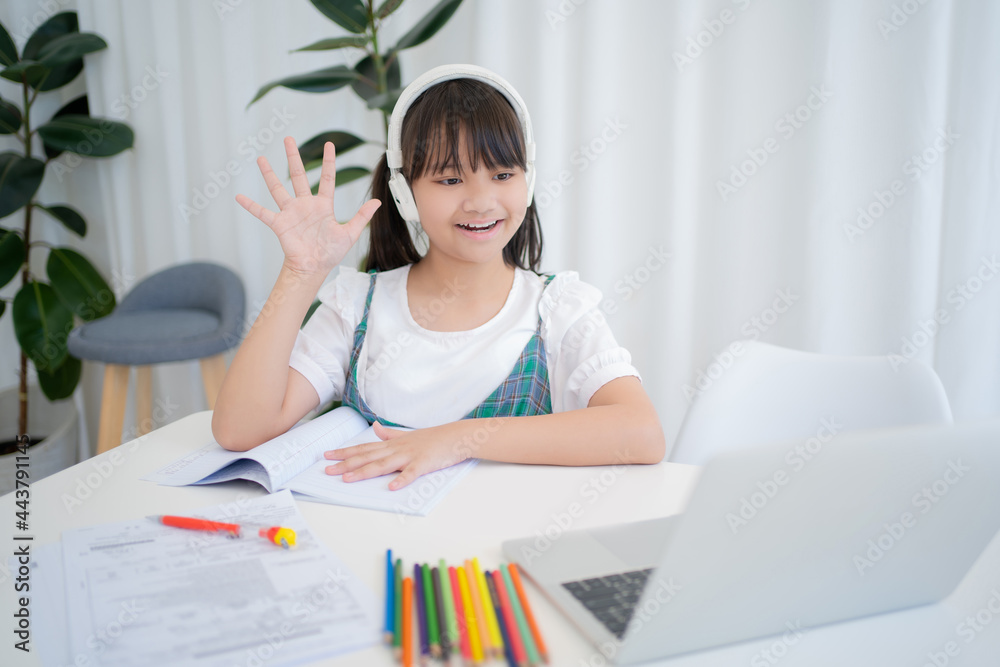 Little children, girls study online at home. She is greeting friends and teachers in the Zoom program with her laptop at home. New Normal. Little children, girls study online at home. She is greeting friends and teachers in the Zoom program with her laptop at home. New Normal.