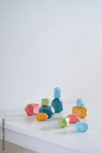 against background of white wall corner of white table. on the table in the center of the frame lie colored wooden cubes of irregular shape toy. place for text. light from the window to the right
