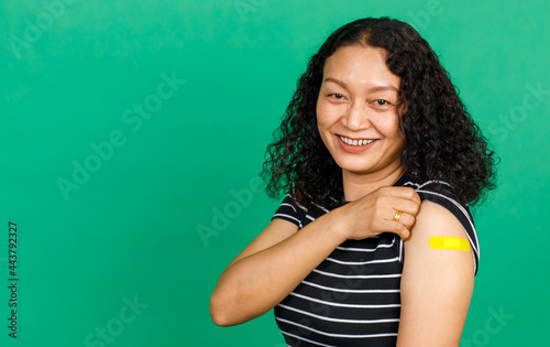 Asian middle aged woman holding her arm with bandage patch showing she got vaccinated for Covid 19 virus on green background. Concept for Covid 19 vaccination © Bangkok Click Studio