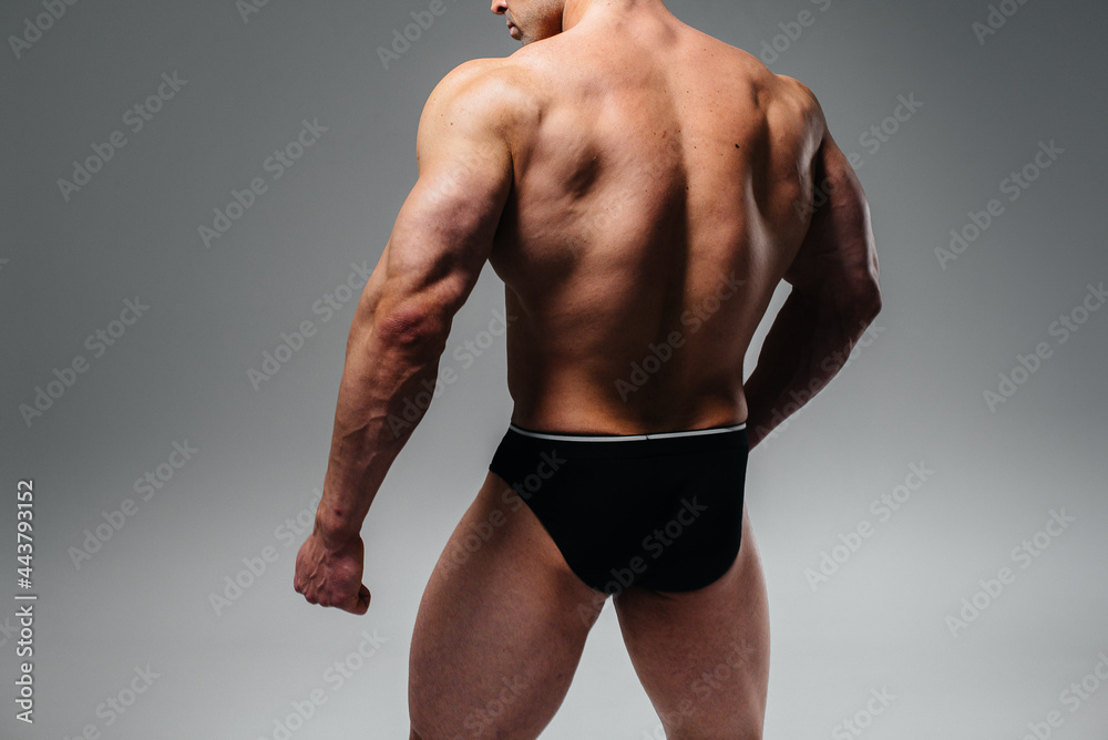 A young athlete bodybuilder poses in the studio topless back. Sport.