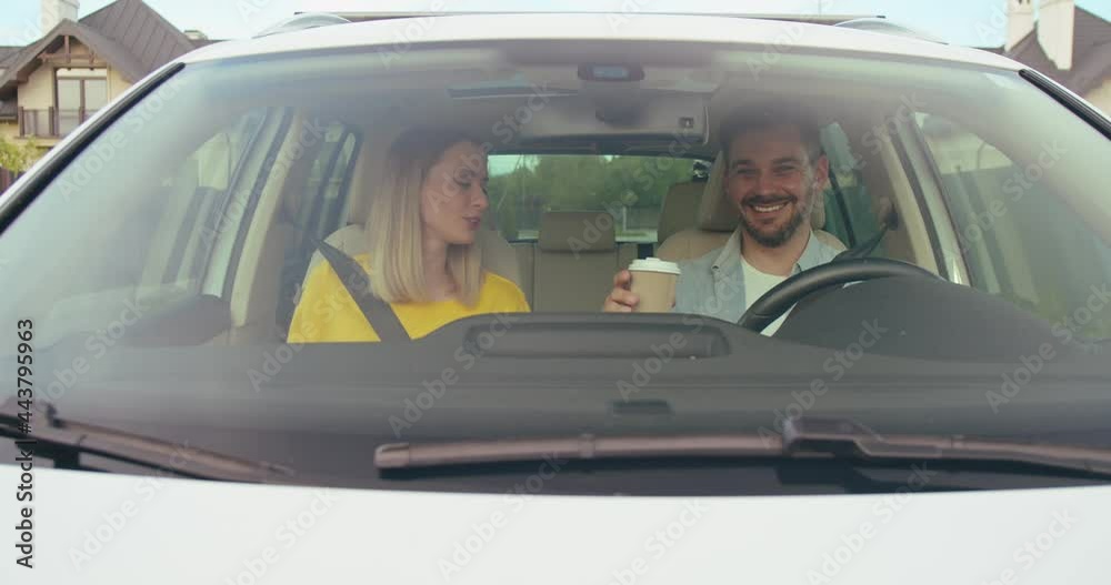 On the way to unknown places. Attractive young woman looking at her husband and giving coffee to him while enjoying the car travel together On the way to unknown places. Attractive young woman looking at her husband and giving coffee to him while enjoying the car travel together