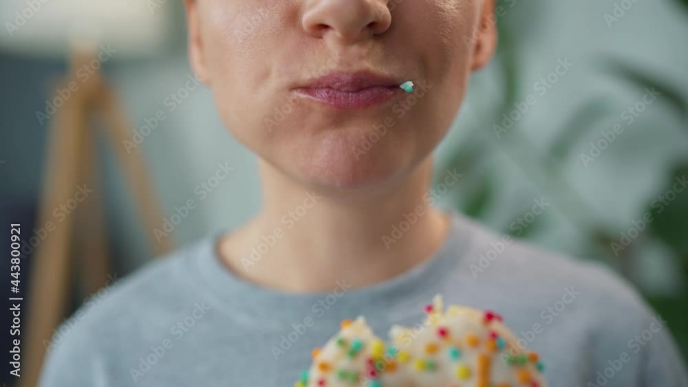 Woman eating a sweet donut in white glaze with multi-colored sprinkles. Close-up