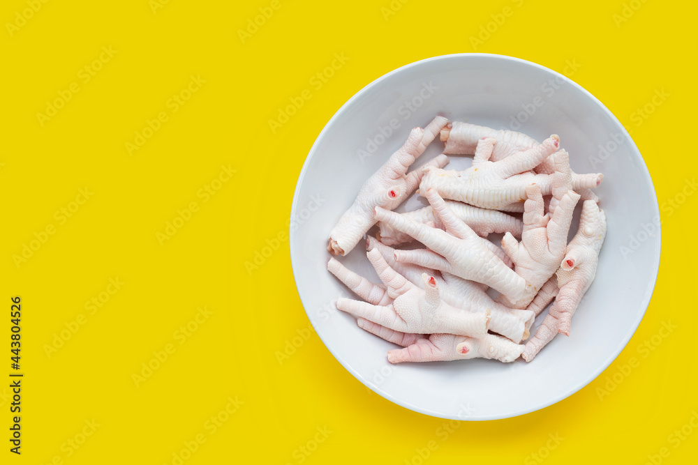 Raw chicken feet in white plate on yellow background Raw chicken feet in white plate on yellow background