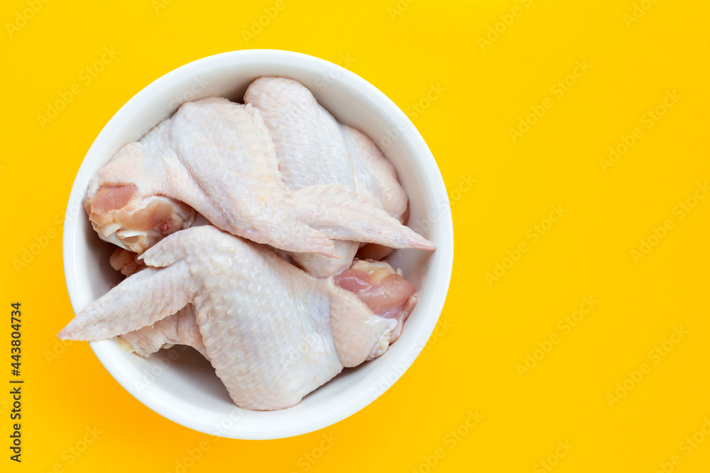 Fresh raw chicken wings in white bowl on yellow background.