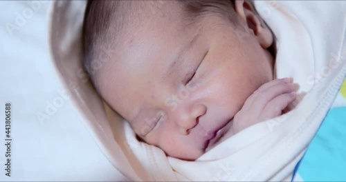 Asian newborn baby girl sleeping peacefully while showing her tiny hand close-up shot. Adorable 0–6-month-old infant extreme close-up with closed eyes. Neonatal first days in life concept. photo