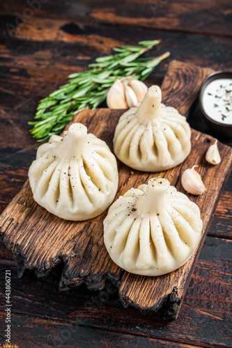 Georgian Khinkali Dumplings with beef and lamb meat on wooden board with herbs. Dark wooden background. Top view