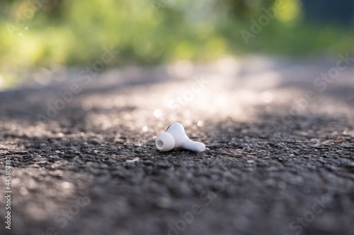 One wireless headphones is lost and lies on the asphalt sidewalk, outdoors. © koldunova