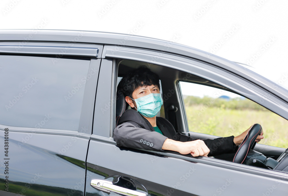 A man wearing a work suit drives a sedan to work in the city. wearing a medical mask to prevent infection during the coronavirus epidemic The driver of the sedan wears a mask for Covid-19.