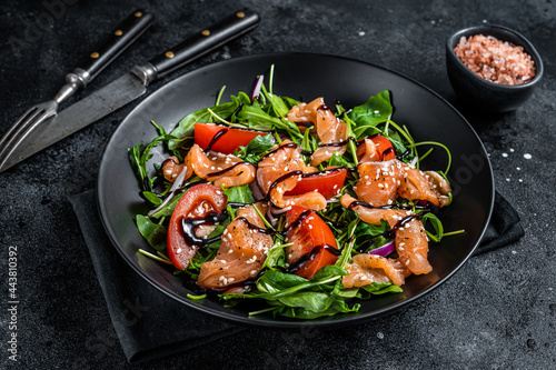 Salmon salad with fish slices, arugula, tomato and green vegetables. Black background. Top View
