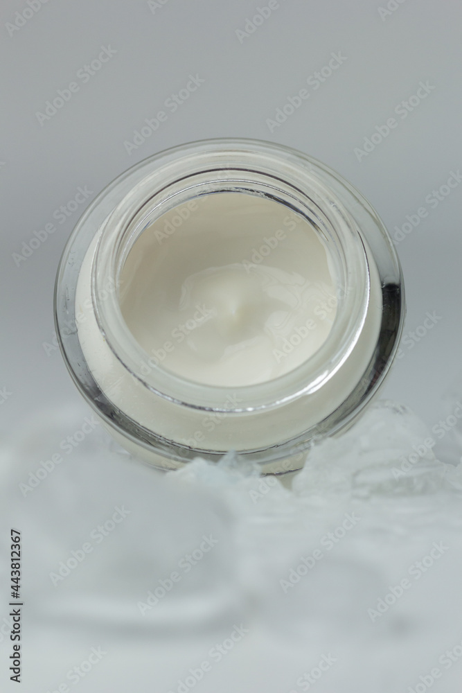 Concept of cooling skin care for summer. Closeup of a jar of moisturizer surrounded by ice.