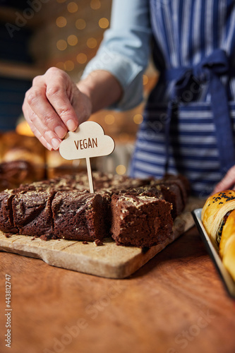Sales Assistant In Bakery Putting Vegan Label Into Freshly Baked Chocolate Brownies