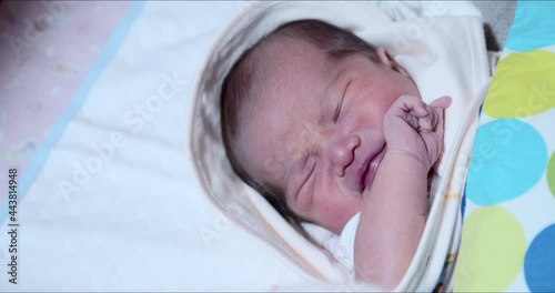Upset Asian newborn baby girl starts to wake up and cry close-up shot. Adorable 0–6-month-old infant with closed eyes. Neonatal care of first days of life concept. photo