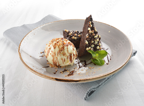 walnut chocolate brownie with vanilla ice cream and peanut, chocolate sauce, mint leaf dessert on round plate western pastry halal menu
