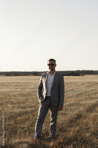 The groom in a suit is standing near his private plane. A male pilot, against the background of an airplane at sunset. © pavelvozmischev