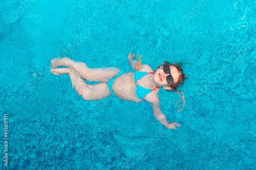 little girl in sunglasses swims in a swimming pool with blue water on a summer day