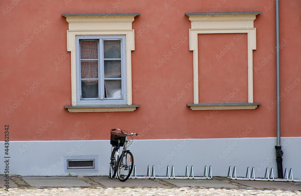 A view of a single tourist bike standing next to a bike parking spot located next to an old yet renovated building and a square covered with stones and boulders spotted in a Polish village in summer