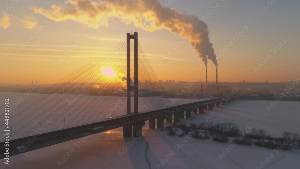 Bridge silhouette over frozen lake or river at sunset (dawn). Low winter sun over industrial landscape with steam from power plant pipes. Haze Bridge silhouette over frozen lake or river at sunset (dawn). Low winter sun over industrial landscape with steam from power plant pipes. Haze