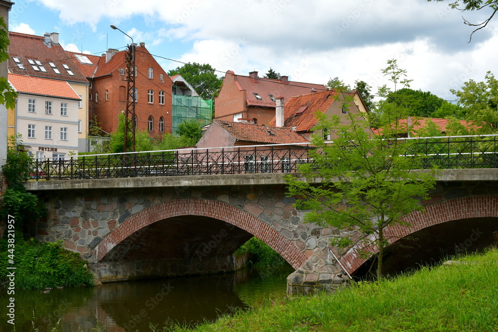 A view of an old abandoned historic buildings with some modern extensions standing in the middle of an old city next to a medieval bridge made out of stone and metal spotted on a Polish countryside