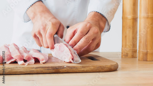 partial view of chef slicing pork tenderloin on chopping board on white